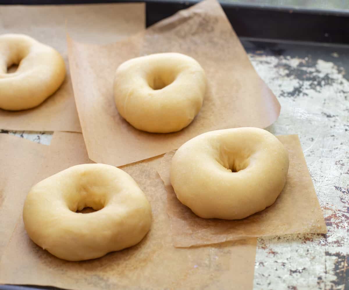 puffy, hand shaped risen donuts on parchment paper squares ready to be fried.
