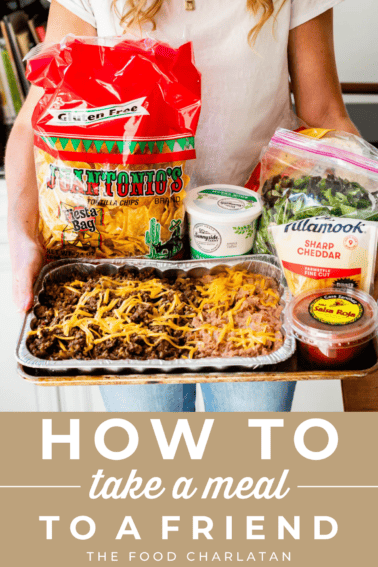 picture of a woman holding a tray of taco meat, beans, chips, and more to take to a friend.