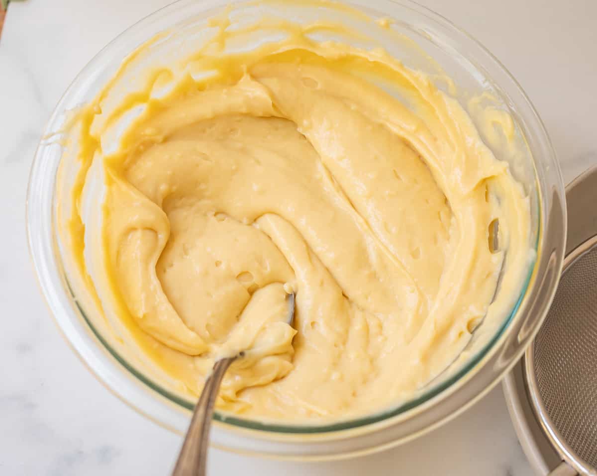 glass bowl filled with chilled, stirred pastry ream with silver spoon in it.