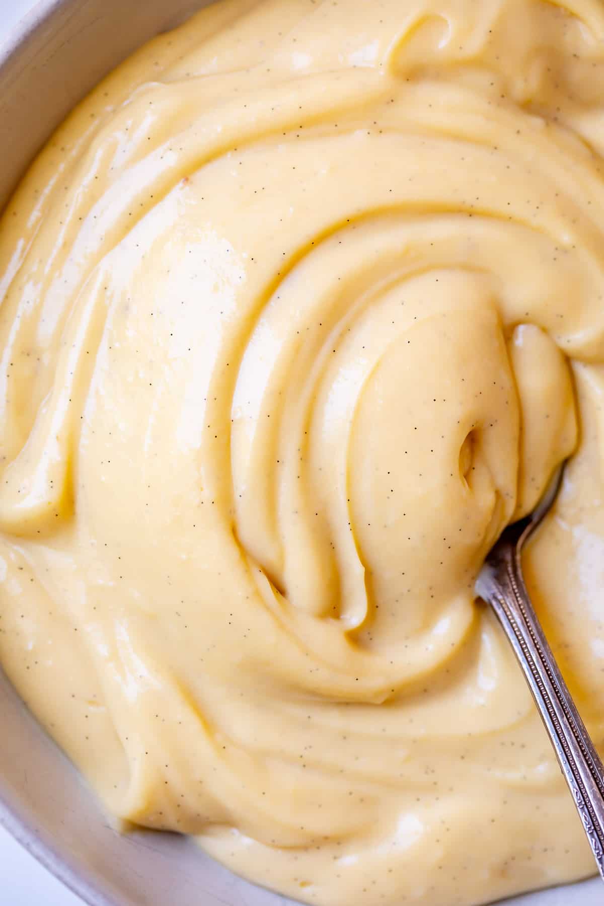 bowl of creamy, vanilla bean flecked Crème Pâtissière being swirled by a spoon.