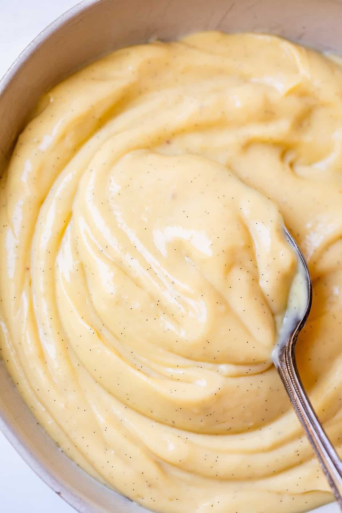 a silver spoon stirring homemade vanilla pastry cream in a bowl.