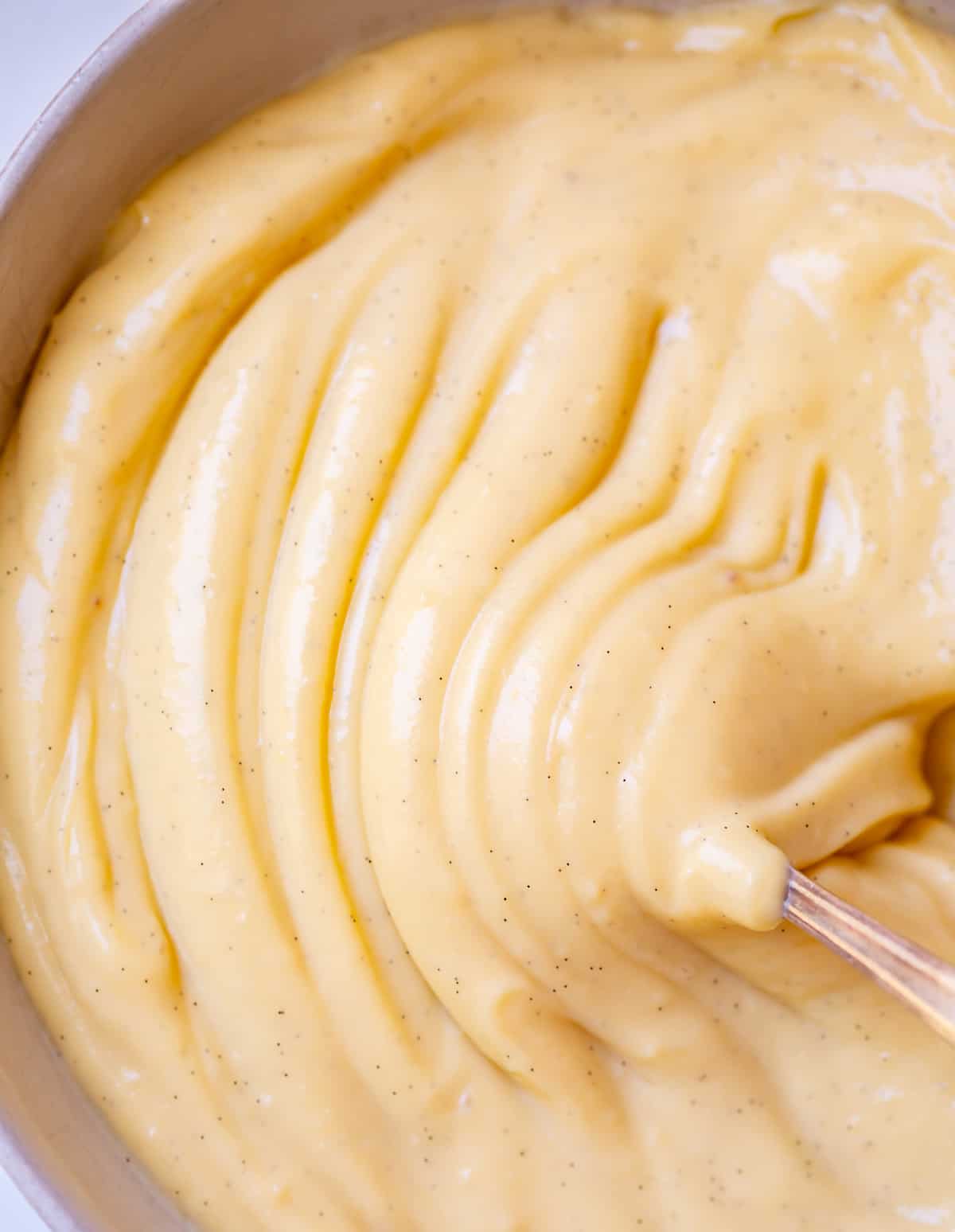 close up of spoon moving through ripples of thick pastry cream in a bowl.