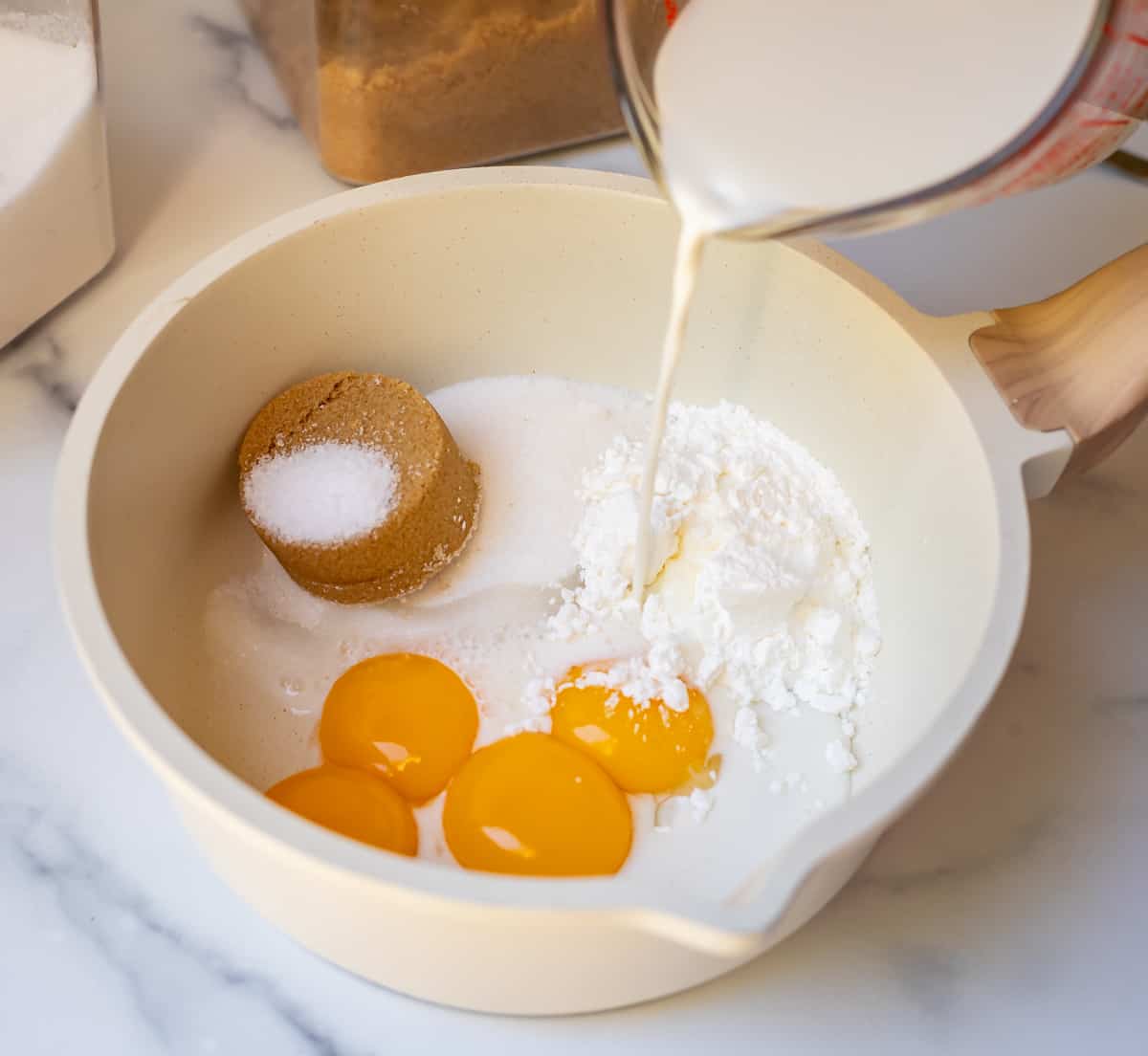 milk being poured into a bowl that has sugar and eggs in it for pastry cream.