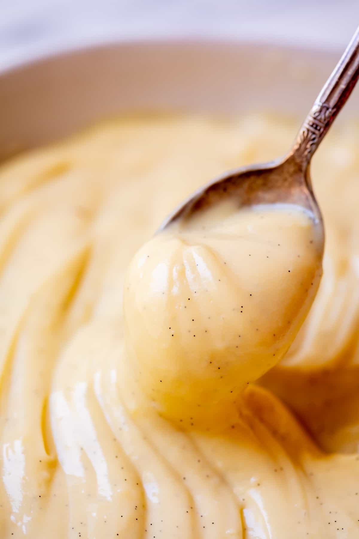 spoon holding up vanilla bean flecked Crème Pâtissière ready to be eaten.