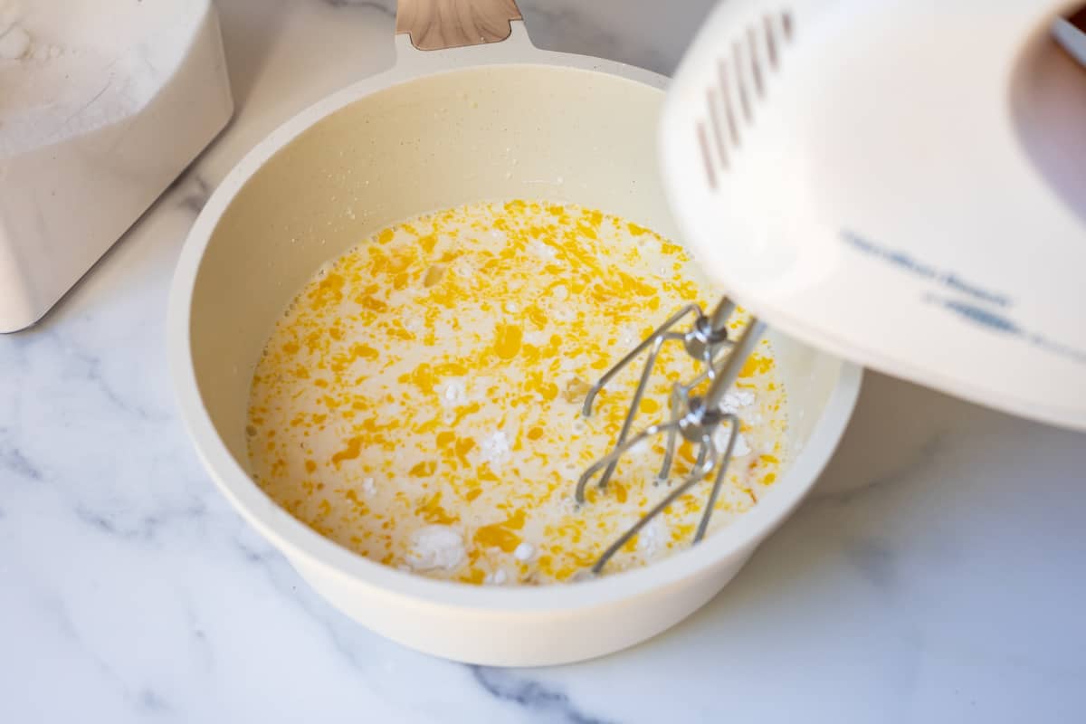 egg, sugars, and milk being mixed by a handmixer in order to make homemade pastry cream.
