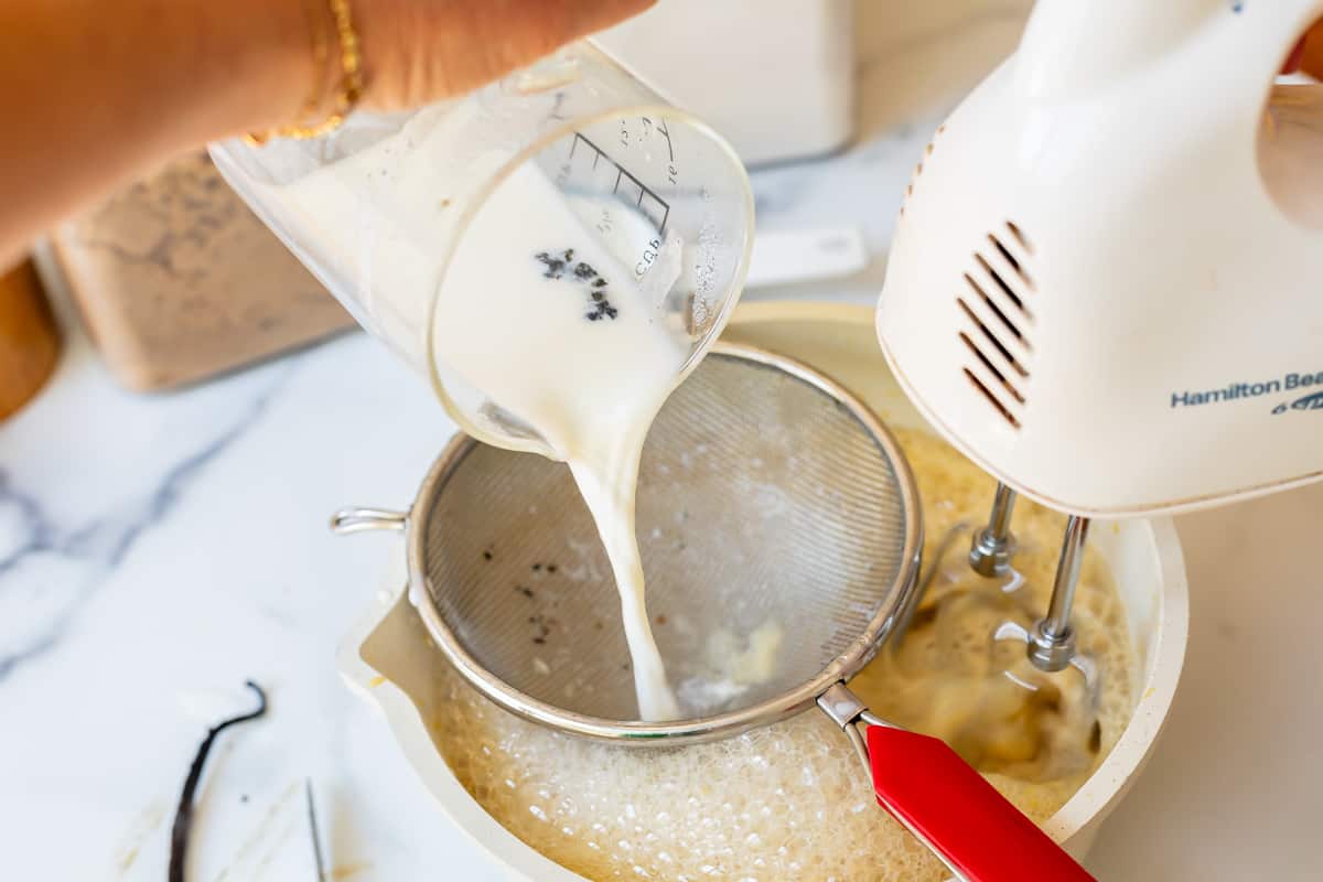 pouring vanilla steeped milk through a sieve into a mixing bowl for creme patisserie.