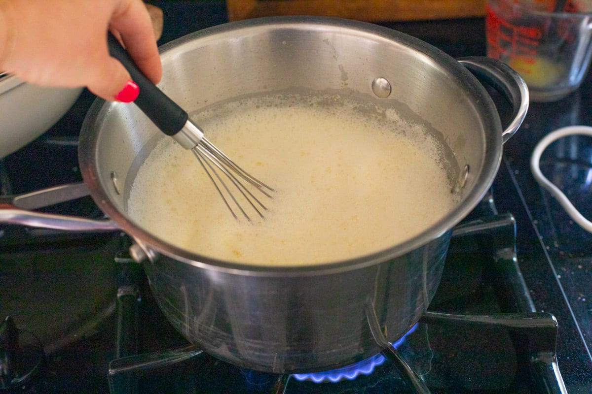 pot with a whisk stirring pastry cream mixture, set over a hot stove to cook.
