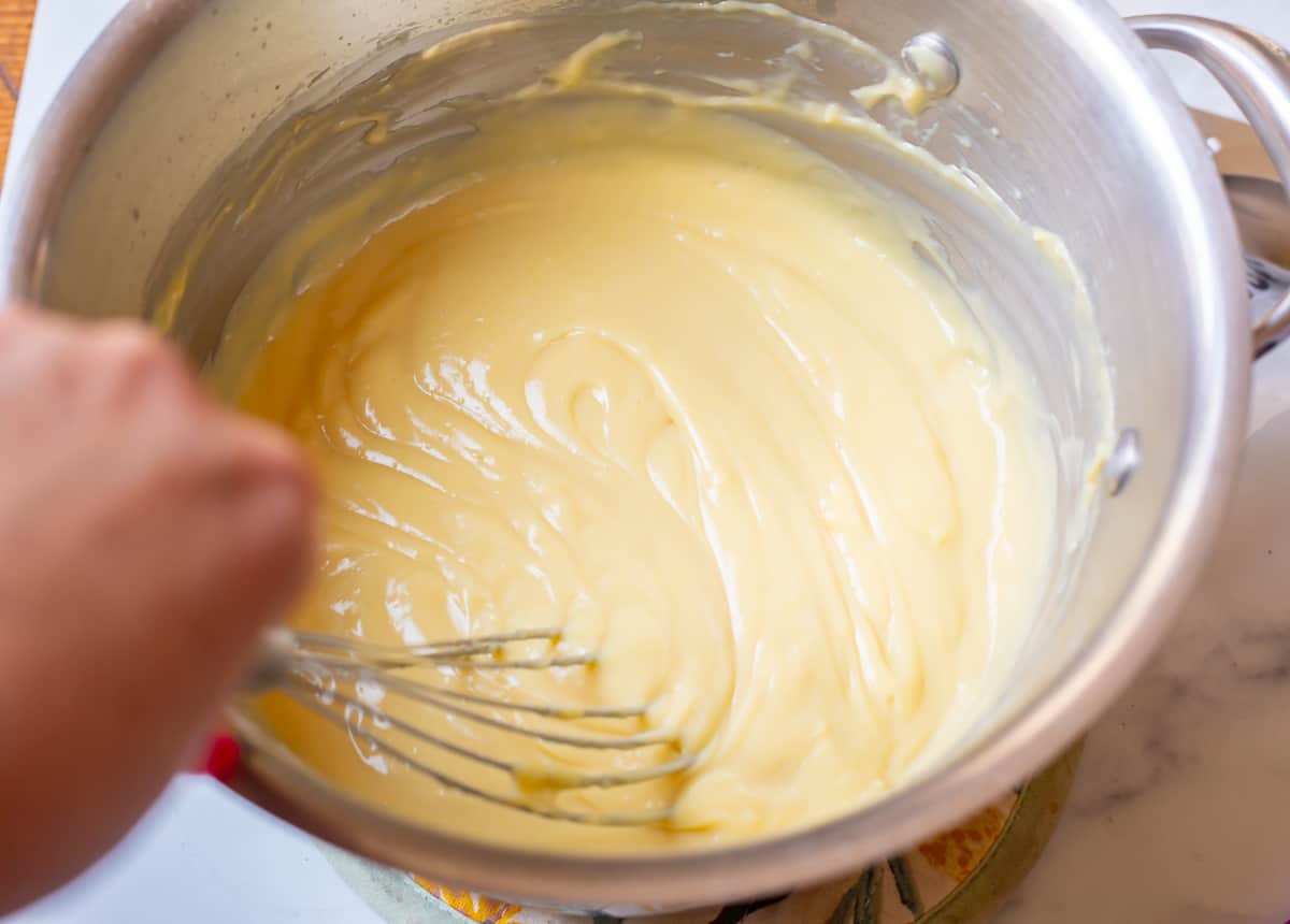 flat whisk stirring through the just thickened pastry cream still in a metal pot.