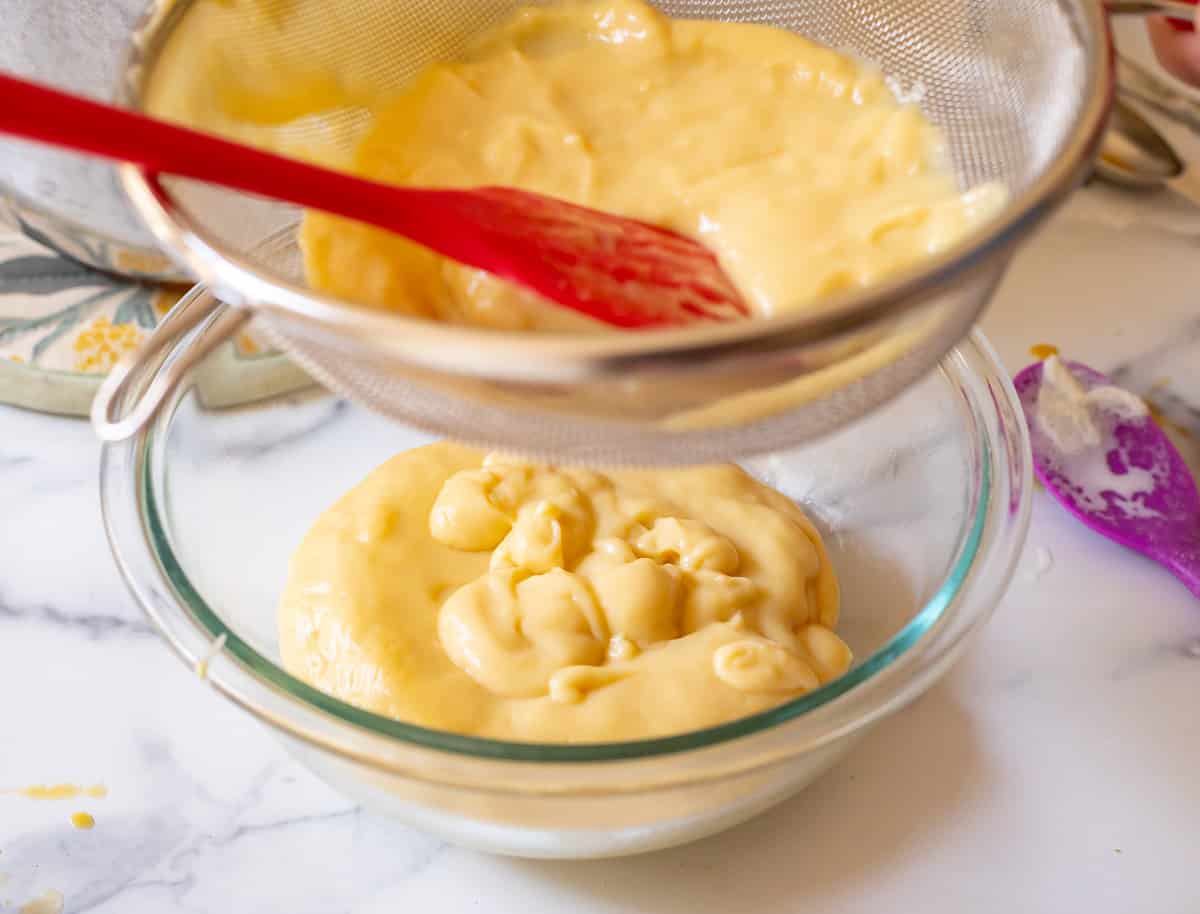 pushing finished pastry cream through a sieve into a glass bowl to make it extra creamy.