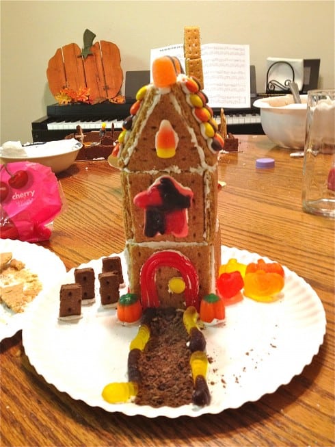 Homemade halloween gingerbread house on white paper plate with candy corn and gum drops.
