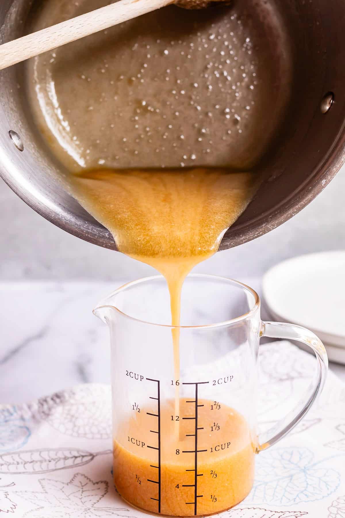 pouring syrup from a pot into a glass measuring cup on a white counter.