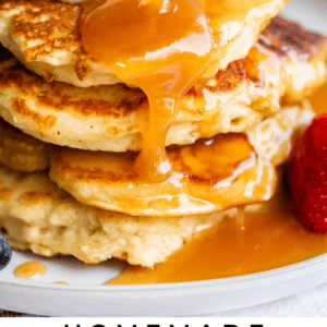 homemade buttermilk syrup being poured over a stack of pancakes on a white plate.