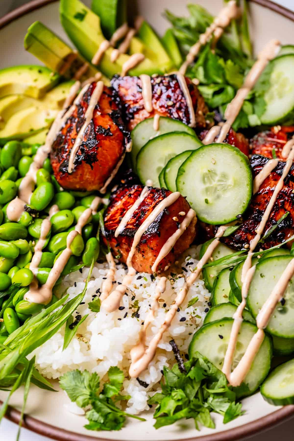 an entire honey sriracha salmon bowl with toppings and seasonings, drizzled with sriracha mayo.