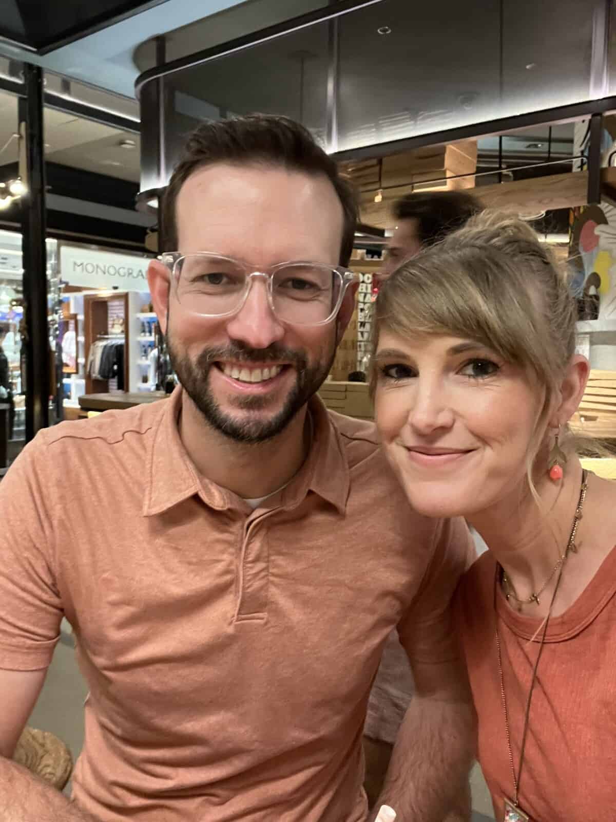 man and a woman smiling at the camera seated in a food court.