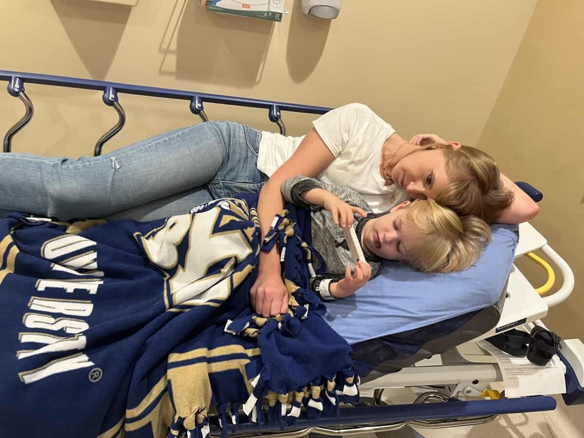 woman and boy on hospital bed watching a phone.