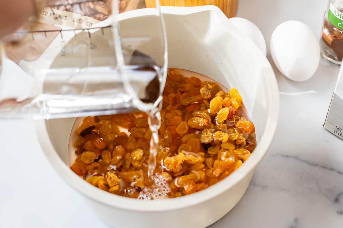 pouring water from a liquid measuring cup over golden raisins in a large bowl.