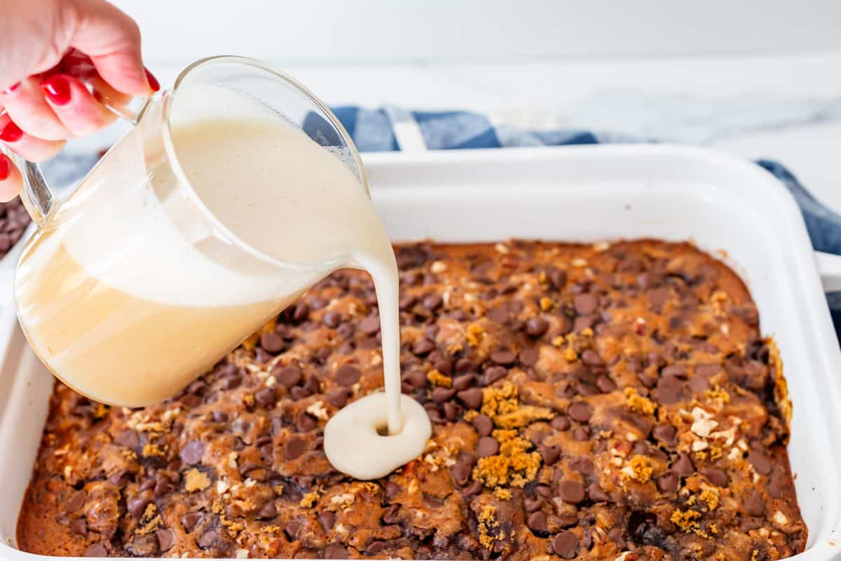 pouring buttermilk syrup from a measuring cup over the top of the baked picnic cake.