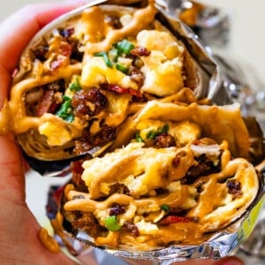 Two breakfast burrito wrapped in foil with sauce on top with bites taken out.