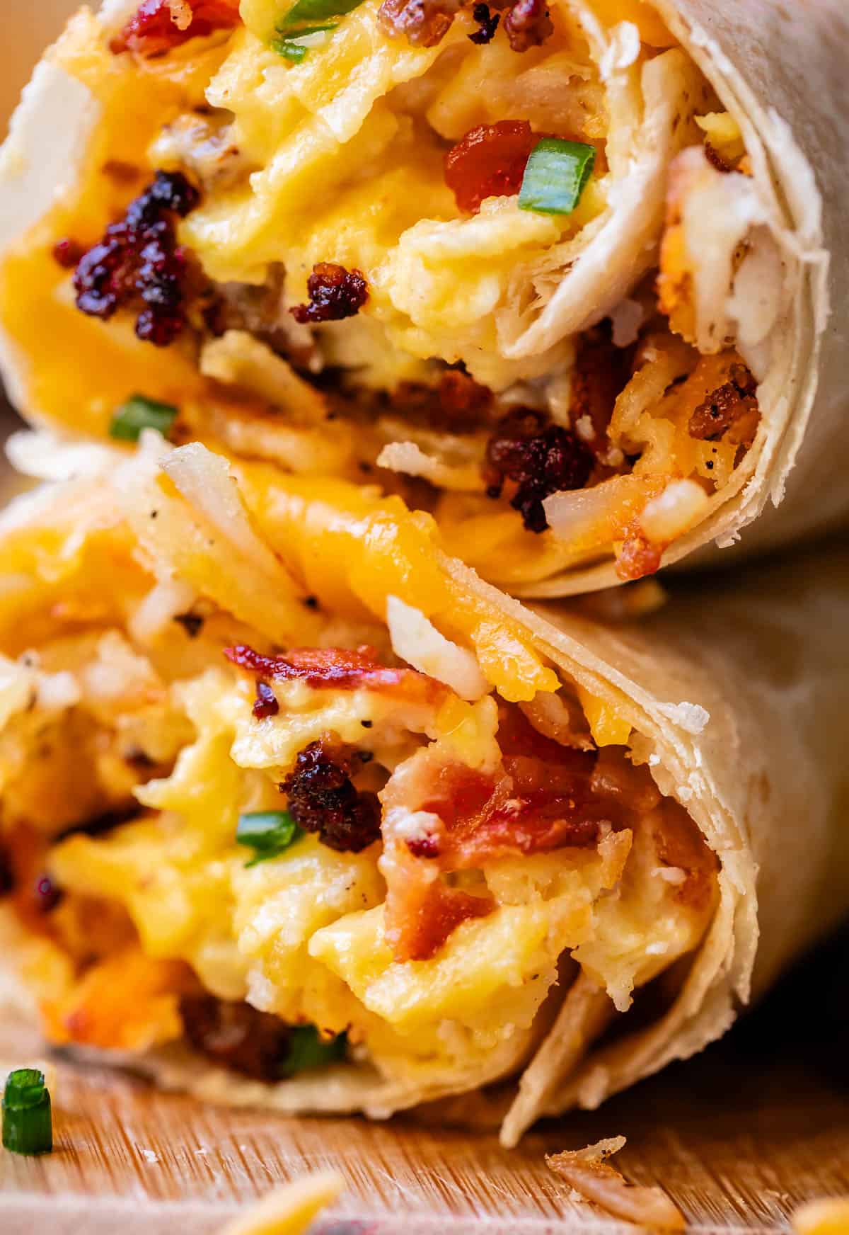 two breakfast burritos stacked on top of each other with cheese.