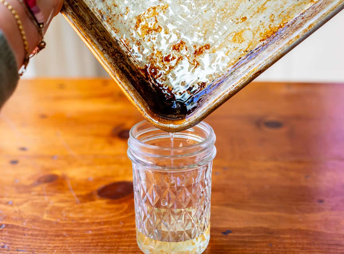 pouring warm bacon grease from sheet pan into a jar for saving to use later.