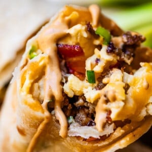 Close-up shot of breakfast burrito with sausage, eggs, bacon, and green onion.