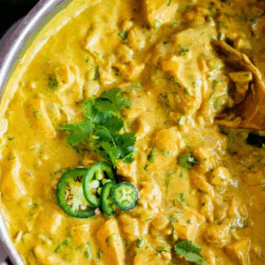 A pot of creamy chicken curry, garnished with fresh cilantro and sliced jalapeños, with a wooden spoon resting in the hearty chicken curry. Text above reads: 30 Minute Chicken Curry.