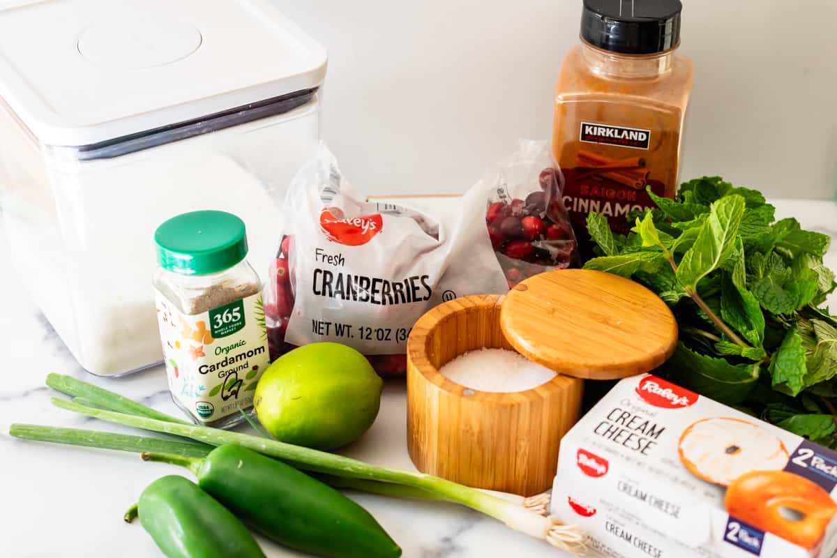 ingredients to make a cranberry dip including jalapeños, lime, cranberries, cream cheese, salt, and sugar.