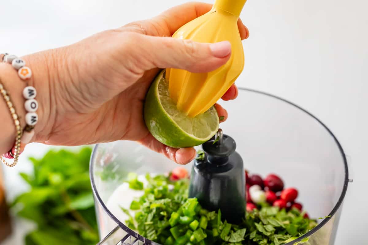 squeezing a lime into a food processor using a citrus reamer by hand.