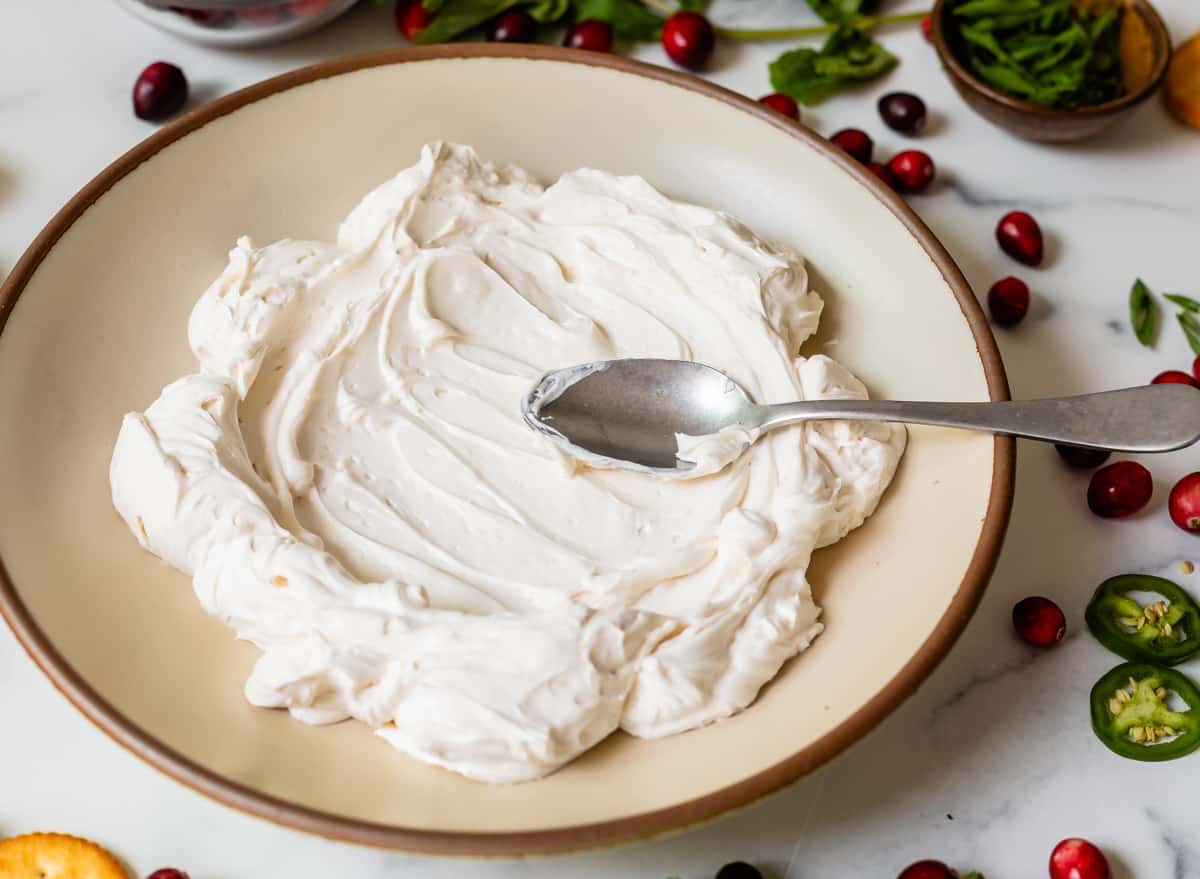 spreading out whipped cream cheese on a wide ceramic plate with a spoon in preparation for a dip to be added.