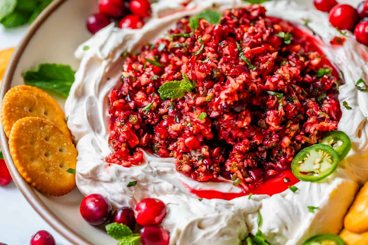 horizontal picture of diced cranberry jalapeño dip on whipped cream cheese with crackers spred out on a plate.