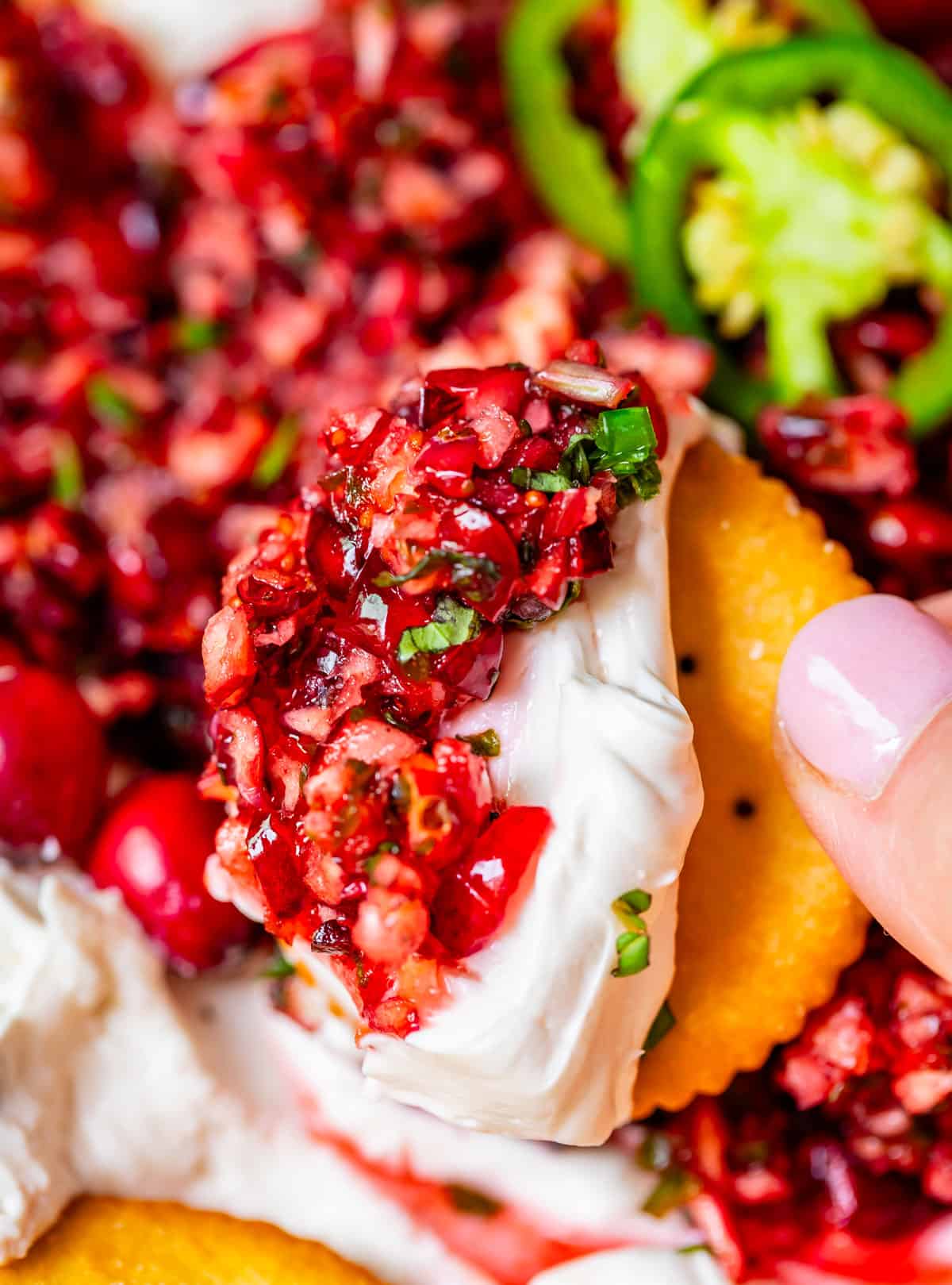 Cranberry Cream cheese dip on a Ritz cracker held up in someone's hand.