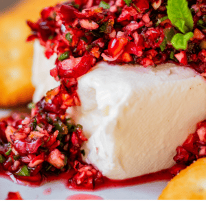block of cream cheese on a plate with cranberry salsa on top, garnished with mint.