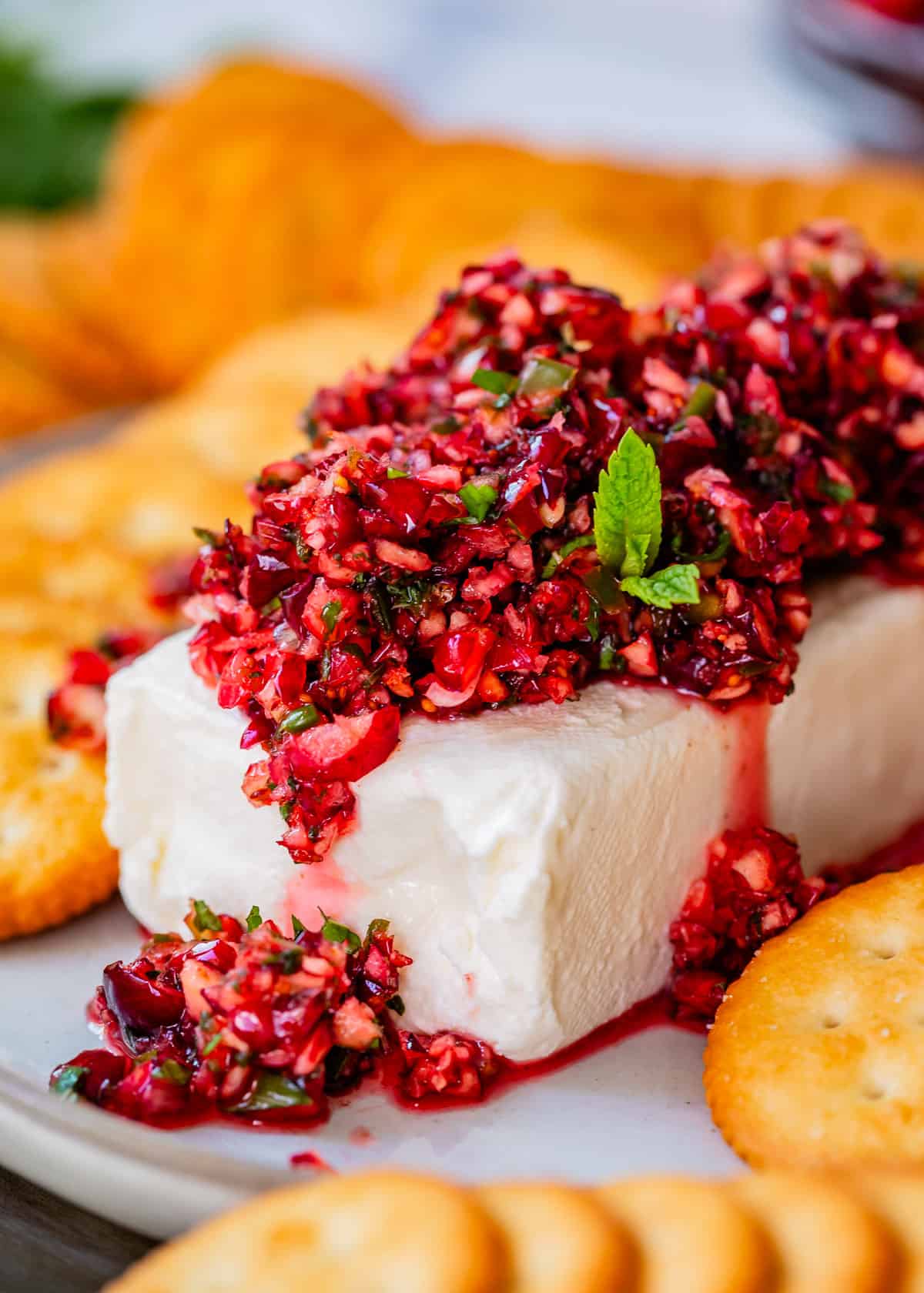 dip with diced cranberries and japaleños on a block of cream cheese on a plate with crackers.