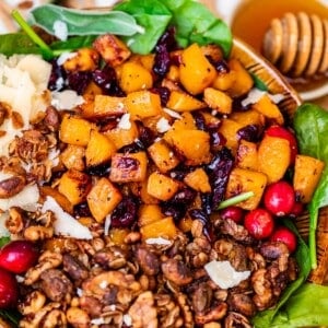 bowl of honey roasted butternut squash salad sitting on a counter with a bowl of honey behind it.