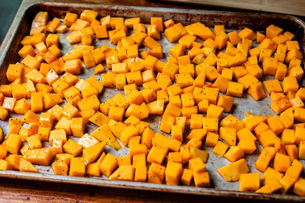 cubed butternut squash in marinade and spread out over a baking sheet ready to cook.