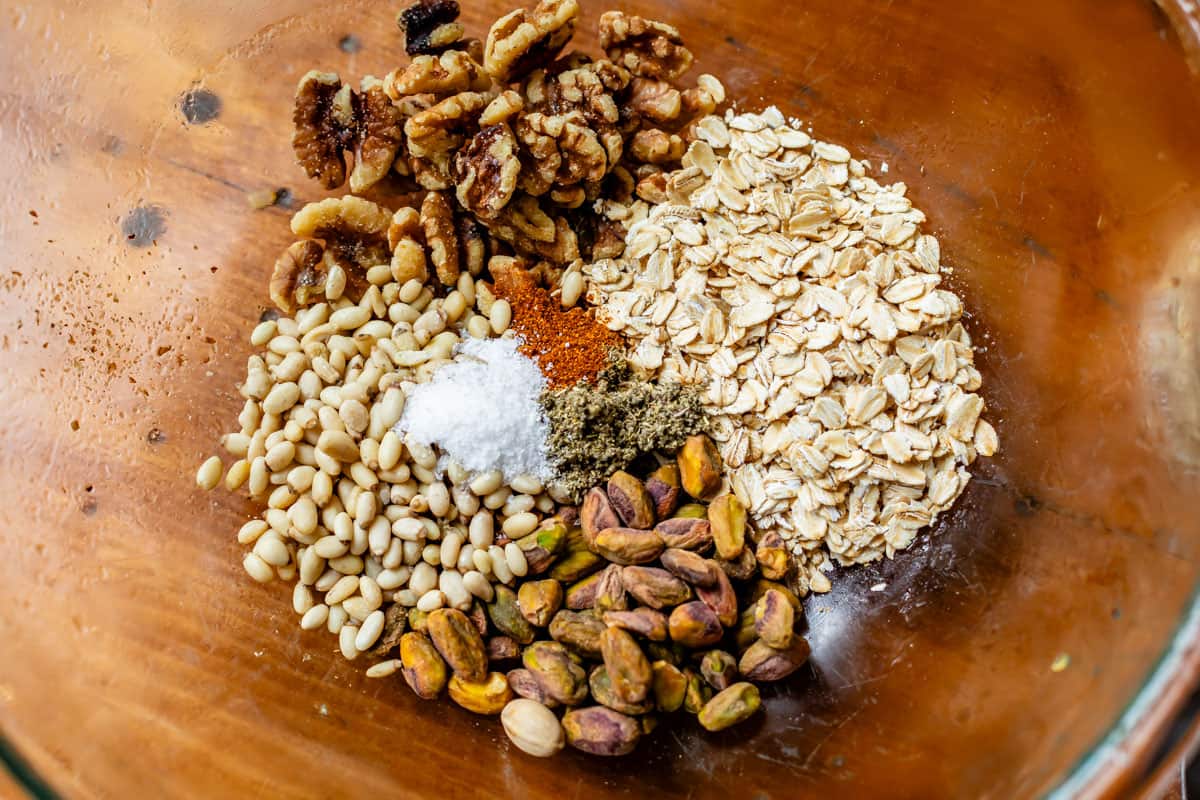 savory granola ingredients in a glass bowl - walnuts, oats, pistachios, pine nuts, and more.