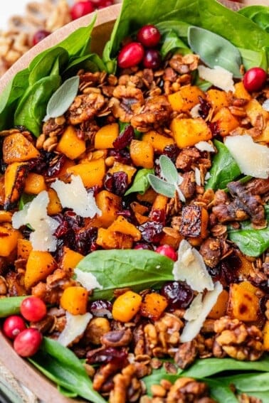 wooden bowl with spinach, roasted squash, cranberries, shaved parmesan, and more.
