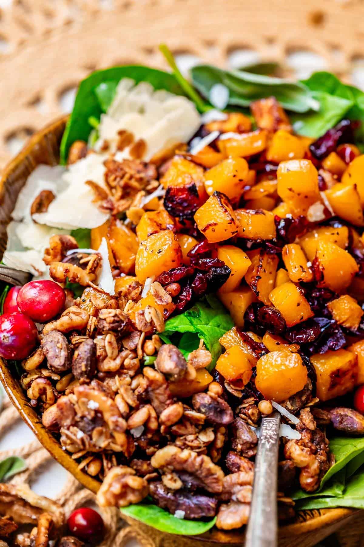 Roasted butternut squash salad in a wooden bowl with a spoon.