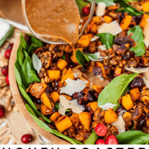 pouring dressing over a butternut squash and spinach salad in a wooden bowl with black handles.