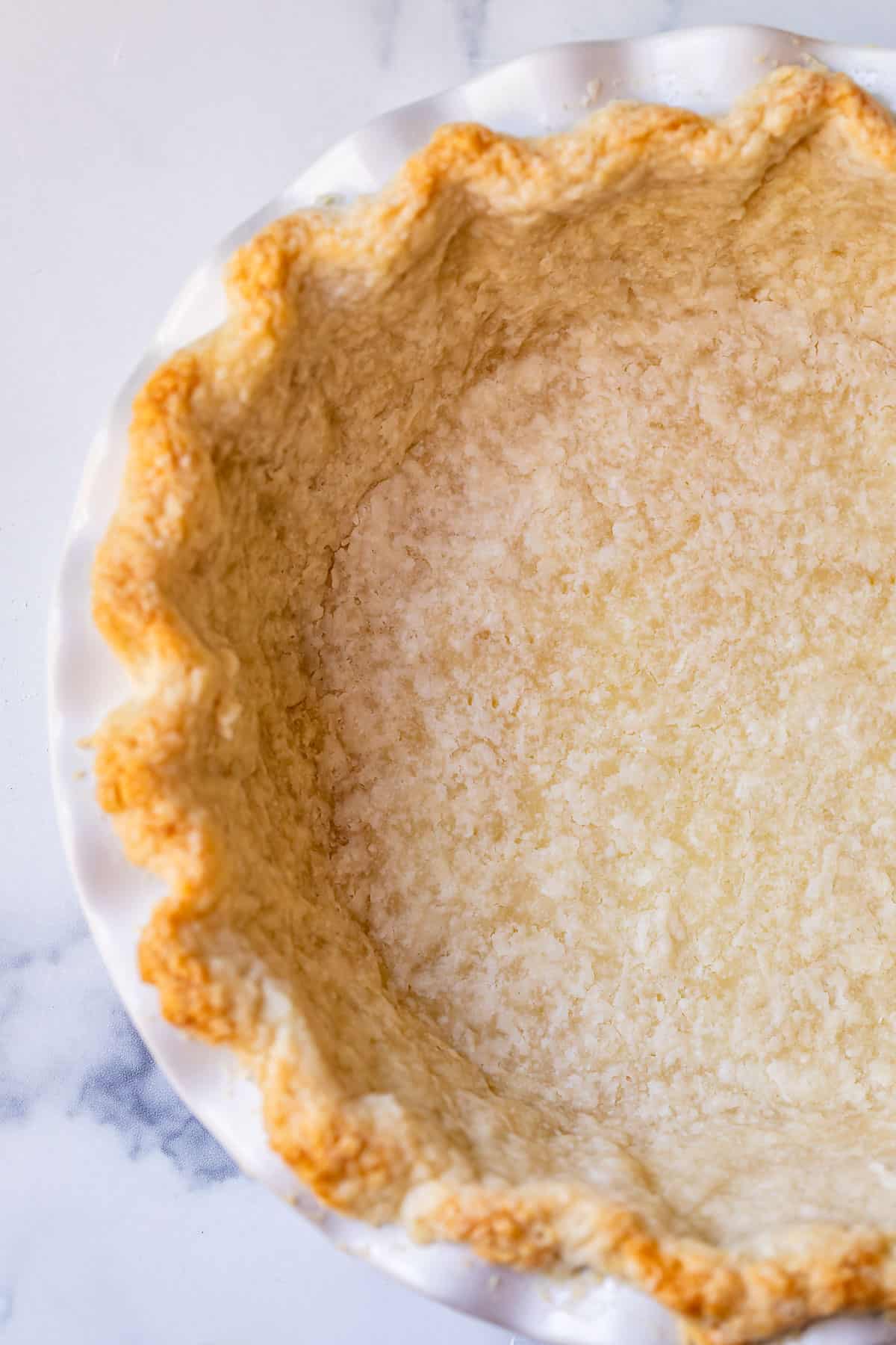 a par baked pie crust in a white pie dish on a counter, overhead.