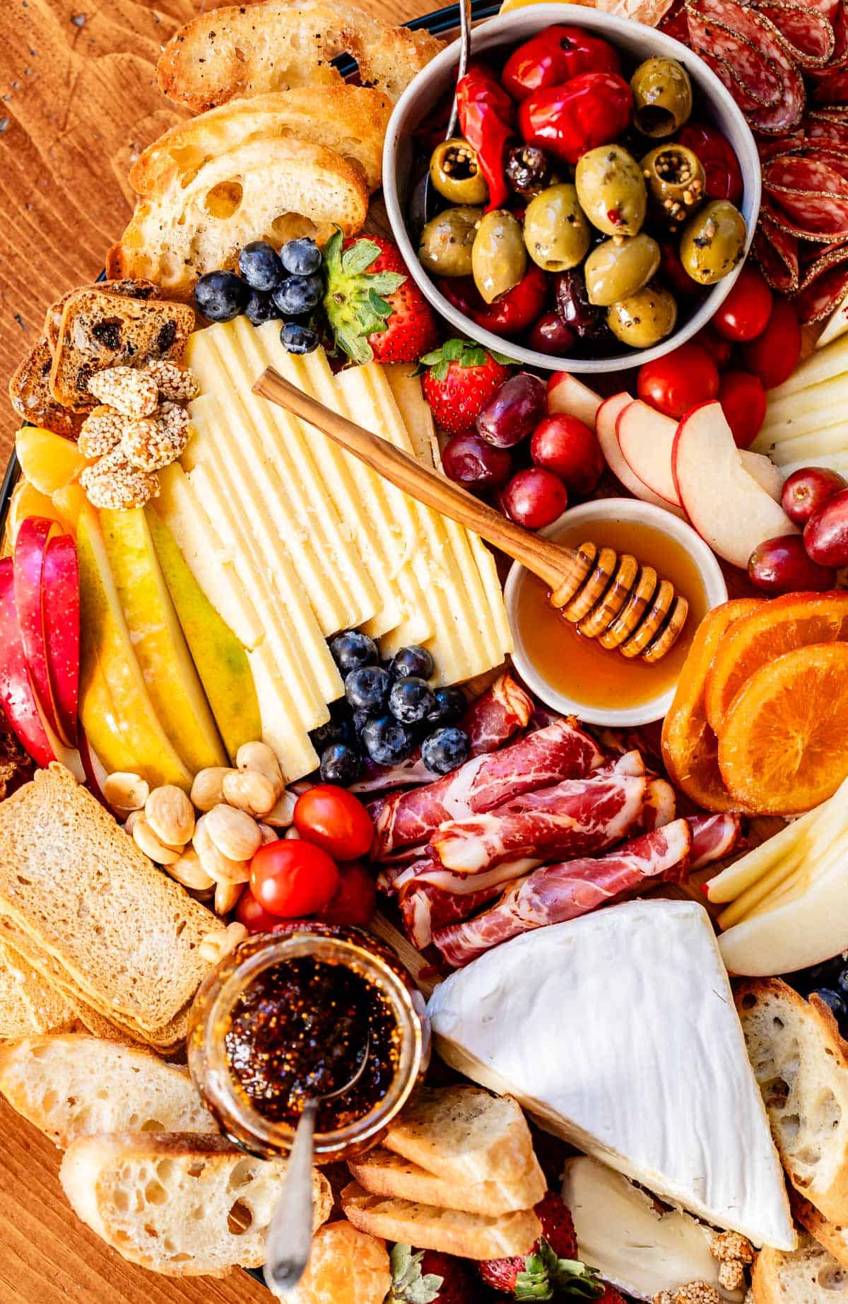 Picture of a charcuterie board with cheese, meat, fruits, honey, oranges, blueberries, etc.