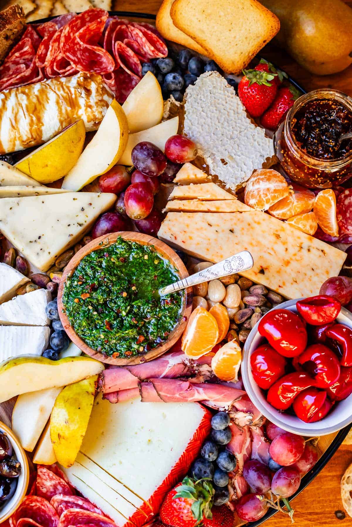 chimichurri on a charcuterie board with cheese, peppers, grapes.