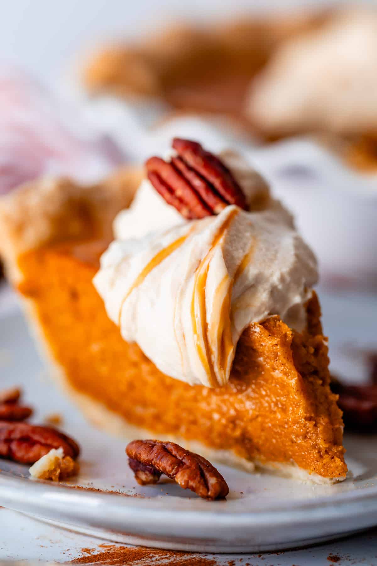 looking straight at a slice of sweet potato pie with salted whipped cream and pecans on a ceramic plate.