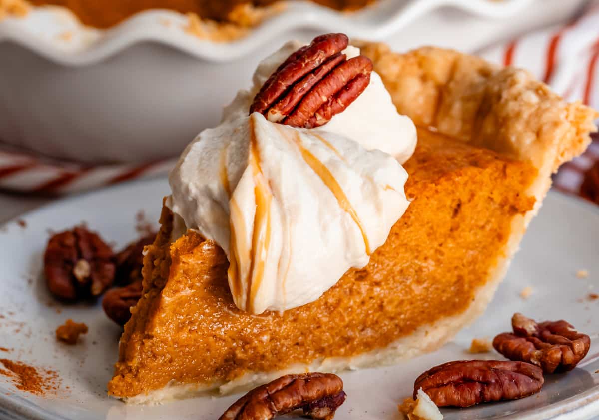side view of a tall slice of sweet potato pie with salted caramel whipped cream and a pecan on top.
