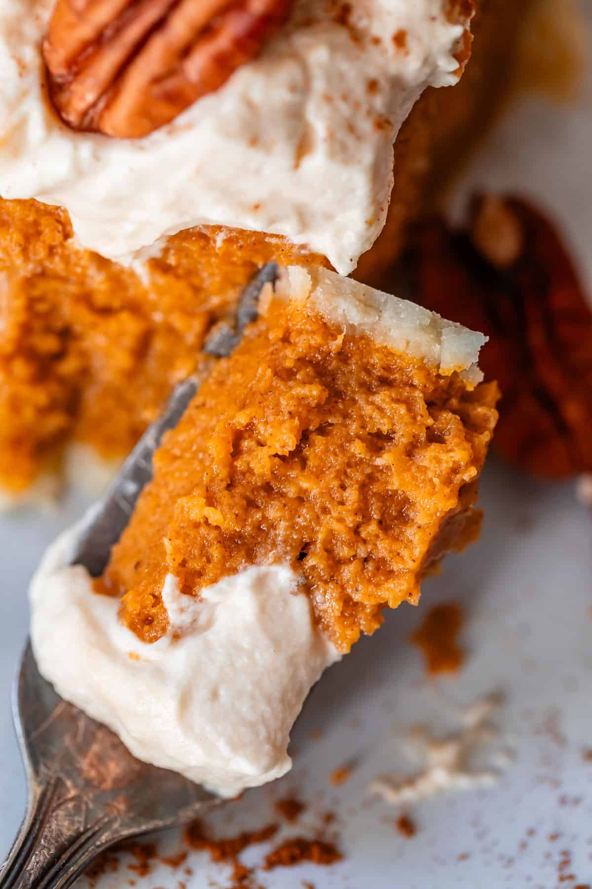 metal fork holding a bite of homemade sweet potato pie with salted whipped cream.