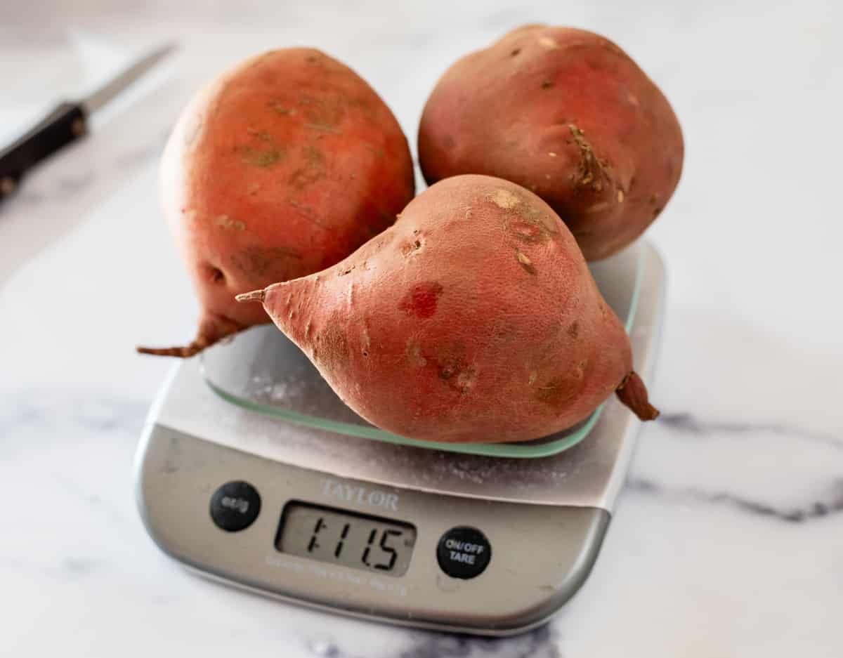 three fat sweet potatoes sitting on a scale with the weight measuring 1 lb 11.5 oz.