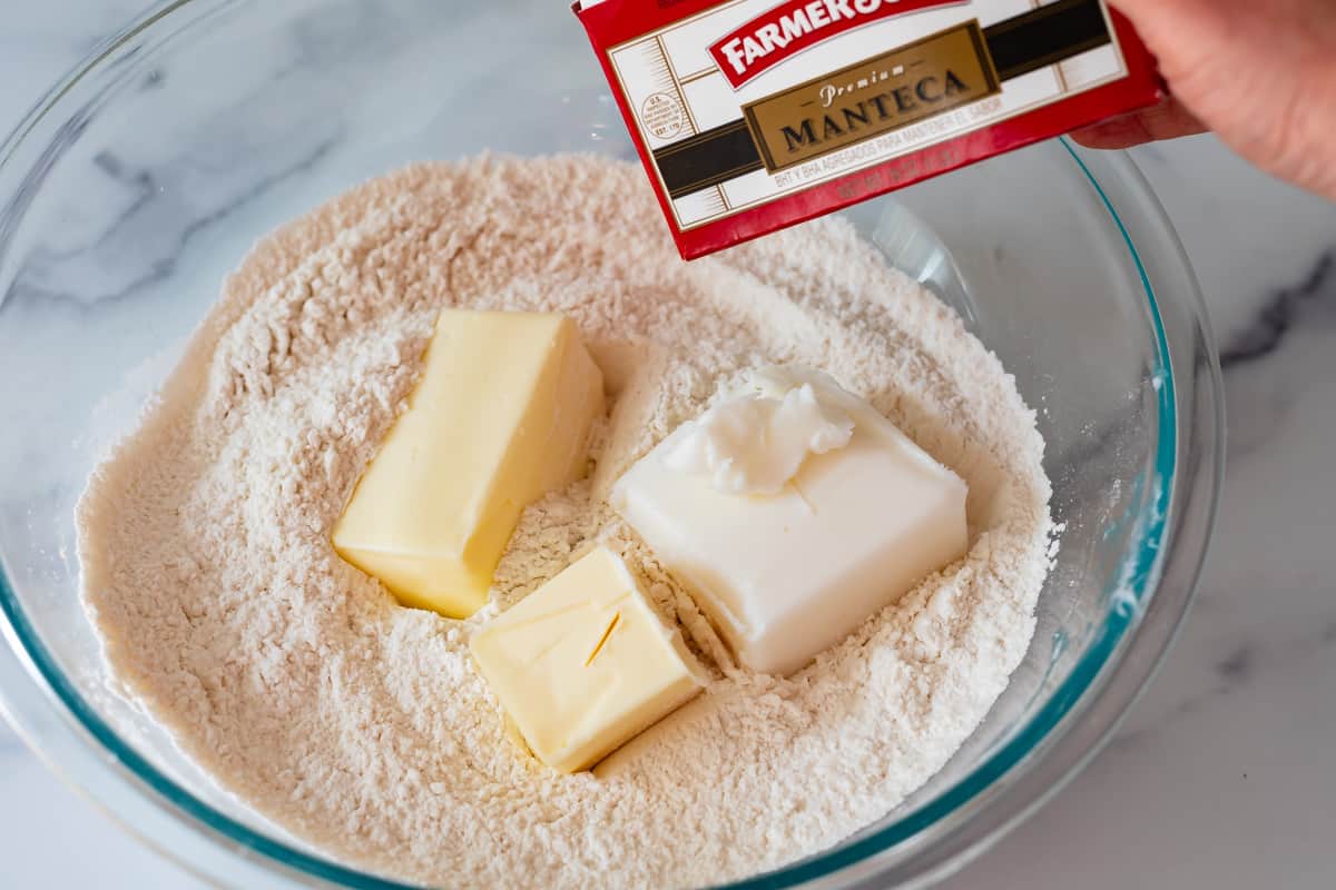 glass mixing bowl with flour mixture with butter and lard dumped on top.