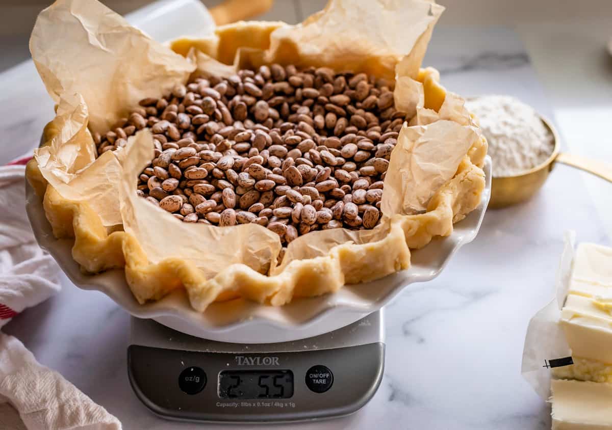 unbaked pie crust on a scale, filled with beans as pie weights.
