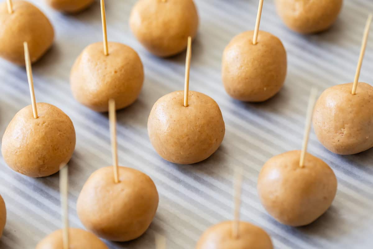 peanut butter dough balls lined on a backing sheet with toothpicks in them ready to freeze.