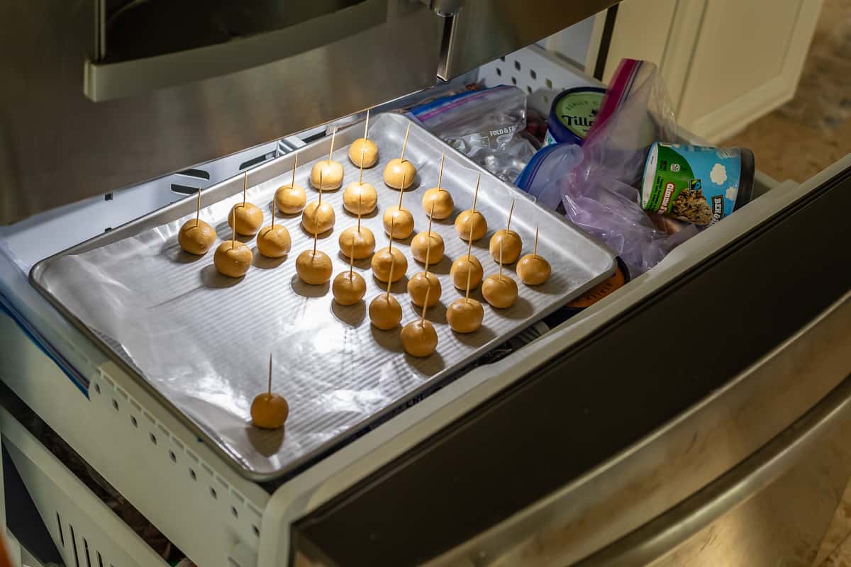 baking sheet filled with peanut butter dough balls with toothpicks in them in the freezer.